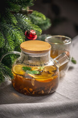 Orange fragrant tea in a glass teapot on the background of a Christmas tree. Cozy warm festive atmosphere