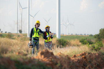 Engineer and worker discussing on a wind turbine farm with blueprints - obrazy, fototapety, plakaty