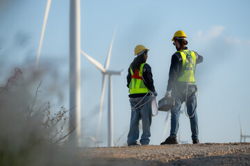 Engineer and worker discussing on a wind turbine farm with blueprints