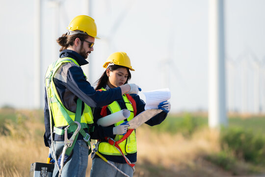 Engineer and worker discussing on a wind turbine farm with blueprints