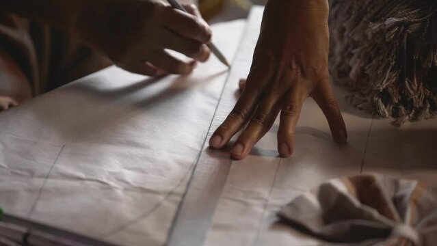 A seamstress is using a steel ruler and pencil to draw a pattern on paper for sewing.