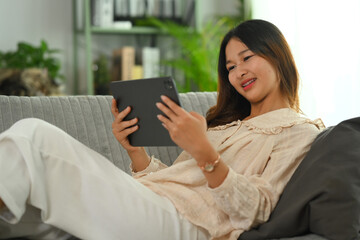 Carefree young Asian woman watching video on digital tablet. People, technology and lifestyle.