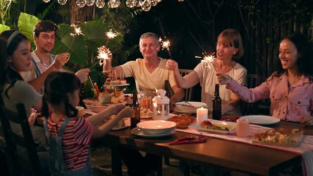 Family and friends gathering celebrating outdoor new year party and play festival sparklers together having enjoy at home. Big family multi-ethnic celebrating outdoors party at garden.