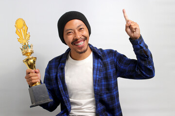 Excited young Asian man, dressed in a beanie hat and casual shirt, proudly raises a finger...