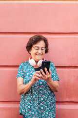 Old woman using smartphone and listening to music with headphones