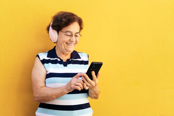 Old woman using smartphone and listening to music with headphones