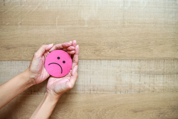 Hand holding red paper cut disappointed face on wooden background. Customer feedback and...