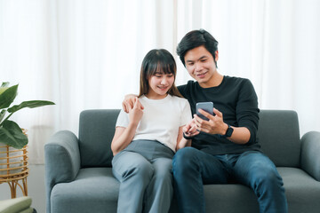 Obraz premium Young Asian couple in love using smartphone together at home.