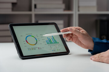 Close-up of a businessman hand analyzing data graph on tablet at workplace.