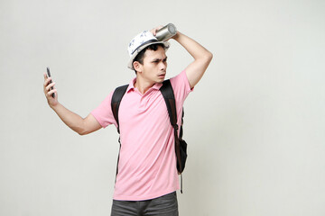 Asian man backpacker hold mobile phone and tumbler bottle with confused expression. travelling concept. on isolated background