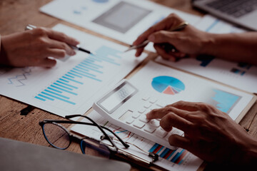 Business meeting with hands pointing at financial charts and a laptop on a wooden table.