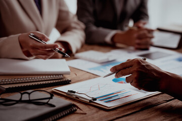 Business meeting with hands pointing at financial charts and a laptop on a wooden table.