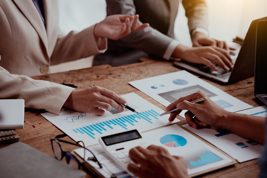 Business Meeting With Hands Pointing At Financial Charts And A Laptop On A Wooden Table.