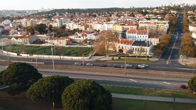 Aerial rotating view of a residential area on the opposite side of Torre Bellem in Lisbon, Portugal. The scene includes a highway with flowing car traffic, low-angle sunlight, high-quality 4K.