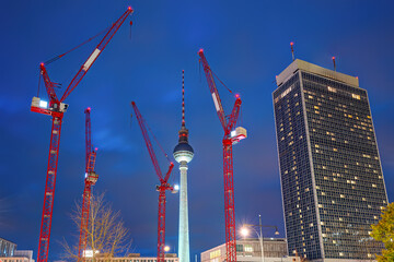 The famous Television Tower of Berlin at night with a skyscraper and four red construction cranes