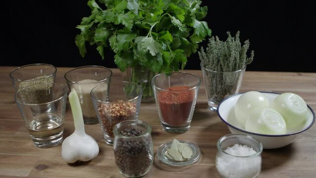 Close up of a wooden table with parsley, onion, pepper, thyme, garlic, cayenne pepper, and rosemary, the ingredients for cafe paris butter