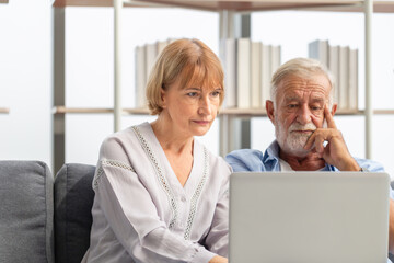 Senior couple using laptop checking their bills, retired elderly family reading documents