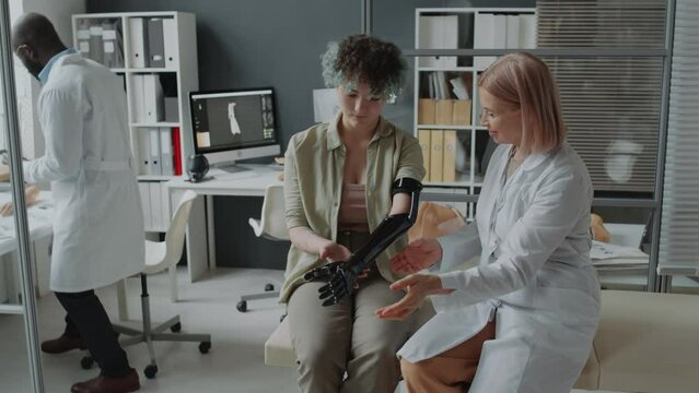 Teenage girl with colourful hair trying on arm prosthetic while female doctor asking its functioning