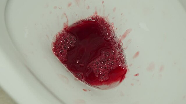 Blood from menstruation cup emptied in toilet and flushed down, close up