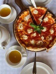 delicious hot sliced ​​Margherita pizza on a served table with cups of tea Photo