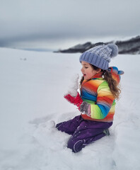 Little girl in snowy nature eating a piece of snow. High quality photo