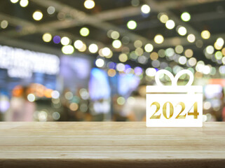 Gift box happy new year 2024 flat icon on wooden table over blur light and shadow of shopping mall,...