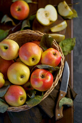 Apples in a basket on a wooden table. Fresh red apples with green leaves on a black background. Fruits. View from above.