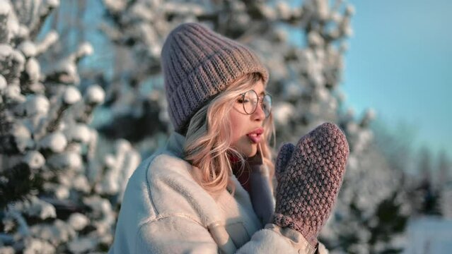 Beautiful young blonde woman feeling cold cool chill shaking mitten at winter forest snowy spruce