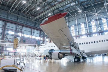 White passenger aircraft in the aviation hangar. Airplane under maintenance. Checking mechanical...