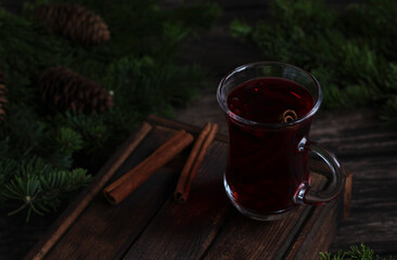 Red mulled wine drink on wooden background with cinnamon, spruce branches and cones