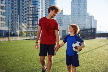 Portrait of tired but happy father and son child walking on football field