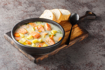 Lohikeitto, salmon fish soup with cream, potato, carrots, leek and dill closeup in a bowl on the serving board. Horizontal