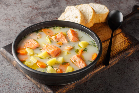 Creamy soup with red fish, potatoes, onions, carrots, celery and green dill in a bowl on the serving board. Horizontal