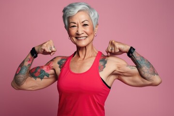 An older woman showcasing her strength by flexing her muscles. This image can be used to promote fitness and healthy aging - obrazy, fototapety, plakaty