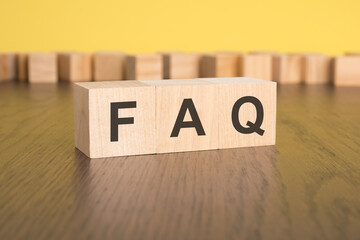 three wooden cubes on a yellow background, with the abbreviation FAQ - Frequency Asked Questions