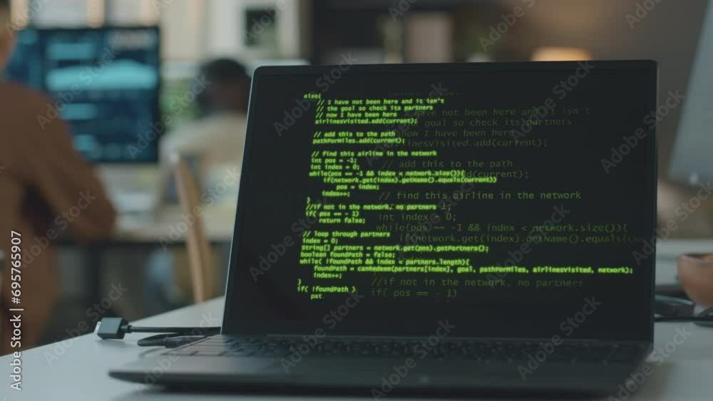 Wall mural closeup of laptop with appearing program code on black screen at table in modern office with two pro