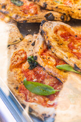 Pizze ripiene di ricotta e prosciutto, condite con sugo di pomodoro, basilico fresco e cotte al forno esposte in una vetrina da vendita di una pizzeria