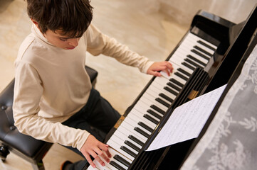 Multi ethnic teenage boy pianist creates music, touches the keys, performs on the pianoforte,...