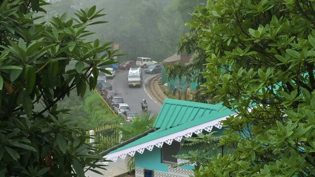 Darjeeling,West Bengal,India - 20.08.2023 : Diesel Toy train passing through curvy Himalayan road. Darjeeling Himalayan Railway, narrow gauge railway. Monsoon clouds passing over green trees.