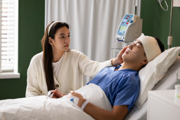 After surgery, the man peacefully dozes in the hospital bed while his wife remains vigilant,...