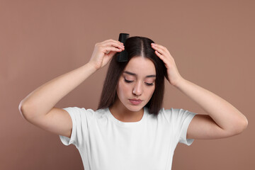 Woman with comb examining her hair and scalp on beige background