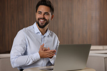 Happy young man with laptop at table in office