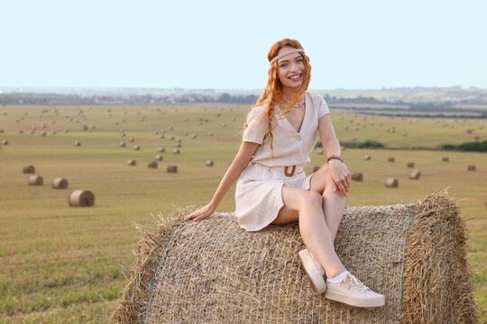 Beautiful hippie woman on hay bale in field, space for text