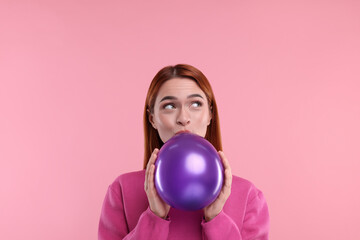 Woman inflating purple balloon on pink background