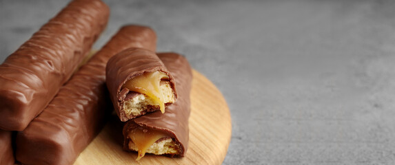 Sweet tasty chocolate candy bars with caramel on grey table, closeup. Banner design with space for text