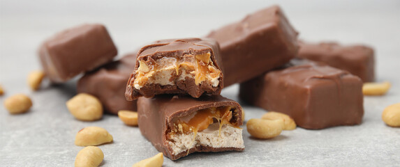 Chocolate candy bars with caramel, nuts and nougat on light grey table, closeup. Banner design