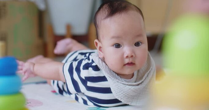 happy little cute Asian baby girl learning trying to crawl on floor with toy in the room, baby exploring home curious infant having fun enjoying childhood