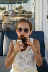 Ritratto di una bambina di nove anni con occhiali da sole e capelli legati mentre mangia un cornetto.