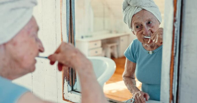 Mirror, reflection and old woman brushing teeth in the bathroom of her home for oral hygiene or dental care. Retirement, health or wellness and a senior person cleaning her mouth with a toothbrush