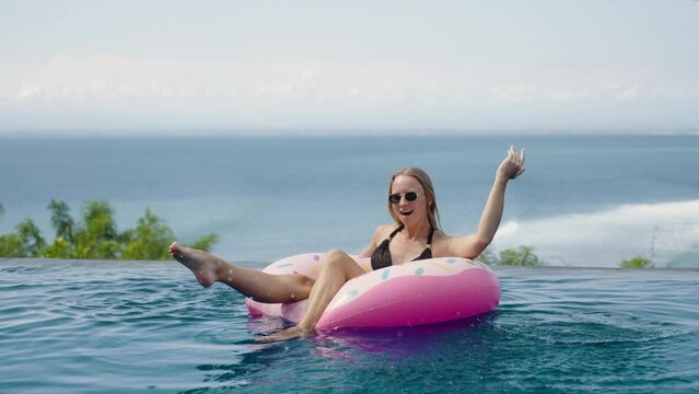 Woman in bikini chill swim on inflatable mattress donut in ocean view infinity pool in luxury private villa. Sunbathing, enjoy on summer vacation trip, rest relax, have fun 